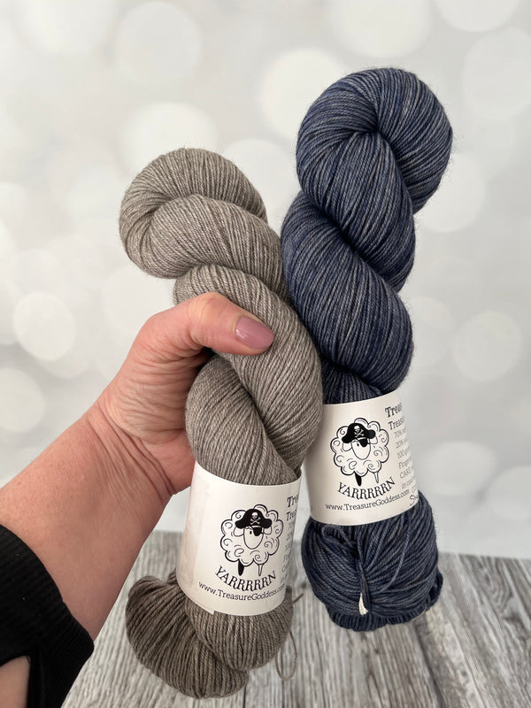 hand dyed Treasured Yak Toes Sock Yarn in natural gray and blue gray held by hand