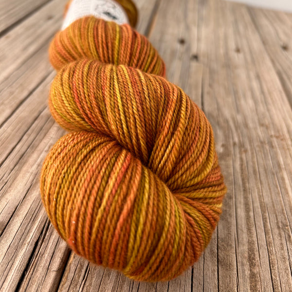 close up of yarn skein with yellow gold orange colors on wood plank